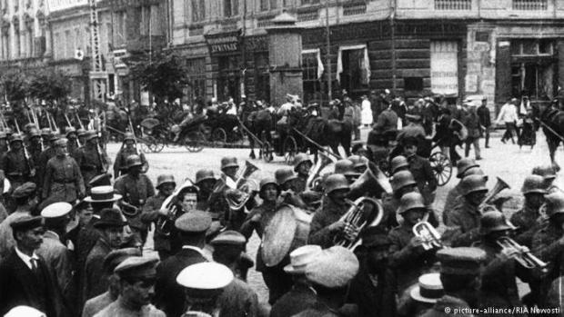 1 березня німецькі війська увійшли в Київ. На цьому фото, зробленому у березні 1918 року, військовий оркестр марширує попереду. Німецькі війська повсякчас влаштовували виступи духових оркестрів та із задоволенням марширували під музичний супровід, часто перед тодішньою міською думою. Зараз це Майдан Незалежності.