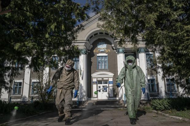 Пожежники в захисних костюмах розпорошують хлор перед лікарнею в Почаєві